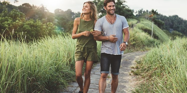 Outdoor shot of young couple in love walking on pathway through grass field. Man and woman walking along tall grass field.