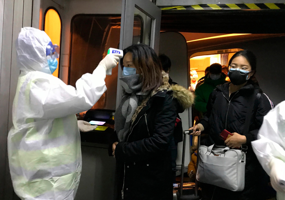 Health Officials in hazmat suits check body temperatures of passengers arriving from the city of Wuhan Wednesday, Jan. 22, 2020, at the airport in Beijing, China. Nearly two decades after the disastrously-handled SARS epidemic, China’s more-open response to a new virus signals its growing confidence and a greater awareness of the pitfalls of censorship, even while the government is as authoritarian as ever. (AP Photo Emily Wang)