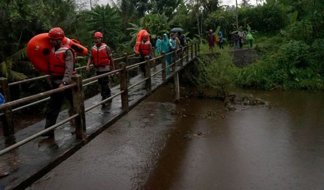 Rescue workers walk past a bridge as they search for students who were missing after a tidal surge swept them away during a school trip, in Sleman