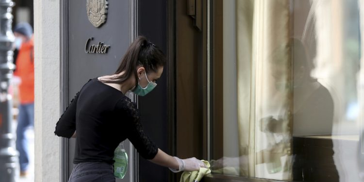 A woman wearing a protective mask cleans a shop window in Vienna, Austria, Tuesday, April 14, 2020. Smaller Austrian shops may reopen with special protective measures from Tuesday on. The Austrian government has moved to restrict freedom of movement for people, in an effort to slow the onset of the COVID-19 coronavirus. The new coronavirus causes mild or moderate symptoms for most people, but for some, especially older adults and people with existing health problems, it can cause more severe illness or death. (AP Photo/Ronald Zak)