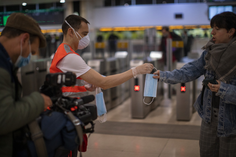 A passenger receives a face mask distributed by a red cross volunteer at the main train station in Barcelona, Spain, Tuesday, April 14, 2020. Face mask distribution in train and bus stations continue as factory and construction workers resume their activities in roughly half of Spanish regions emerging from the Easter holiday period. Spain's left-wing Cabinet is expected to pass new measures to aide smaller business and the self-employed affected by the freezing of economic activity. (AP Photo/Emilio Morenatti)