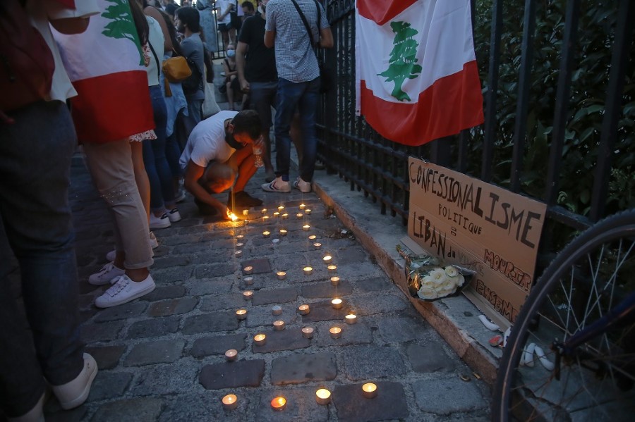 A man of the Lebanese community lights a candle next to a Lebanese flag during a vigil in memory of victims of the deadly blast in Beirut in Paris, Wednesday, Aug. 5, 2020. French President Emmanuel Macron is traveling to Lebanon on Thursday to offer support for the country after a massive, deadly explosion. (AP Photo/Michel Euler)