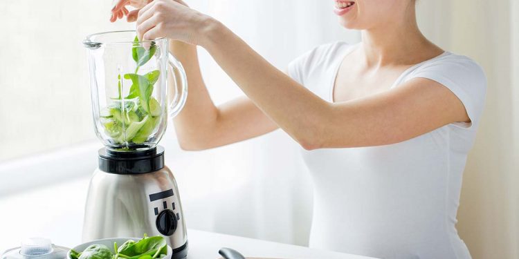 close up of woman with blender and vegetables