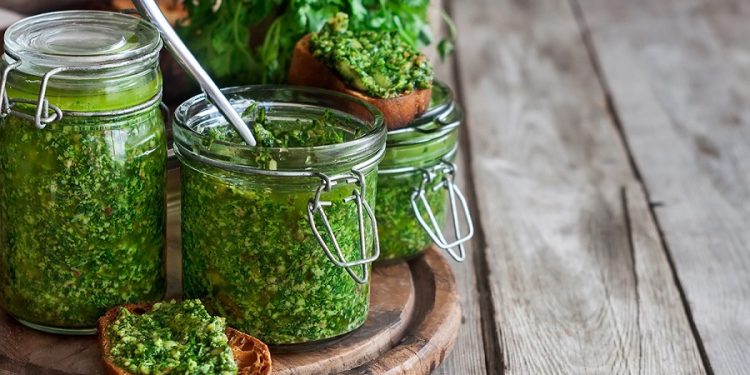 Homemade cilantro pesto in jars on wooden background