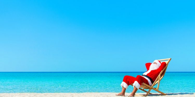 Christmas Santa Claus resting on sunlounger at ocean sandy tropical beach - xmas travel vacation in hot countries concept