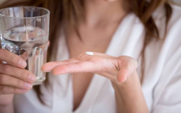 depositphotos_211585658-stock-photo-woman-holding-pill-and-glass-600x400
