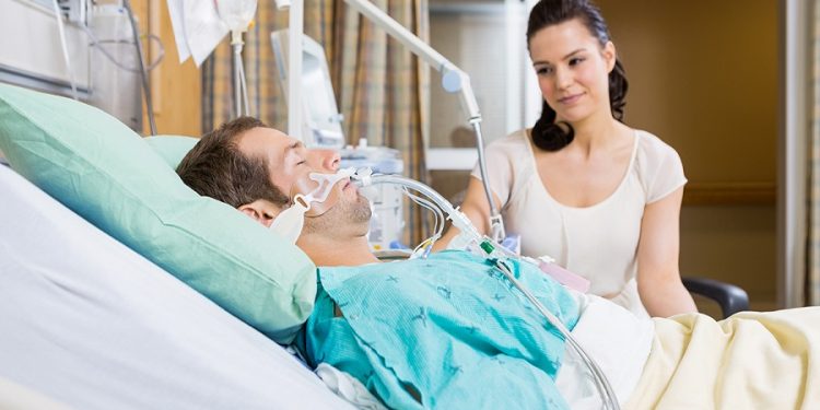 Beautiful woman looking at man lying on bed in hospital