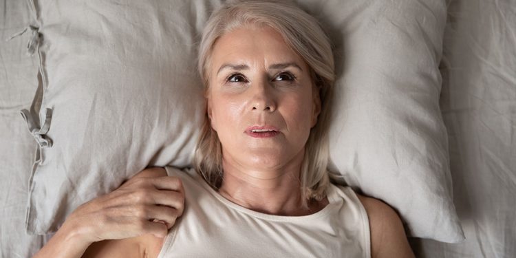 Middle aged woman insomniac lying awake in bed, top view