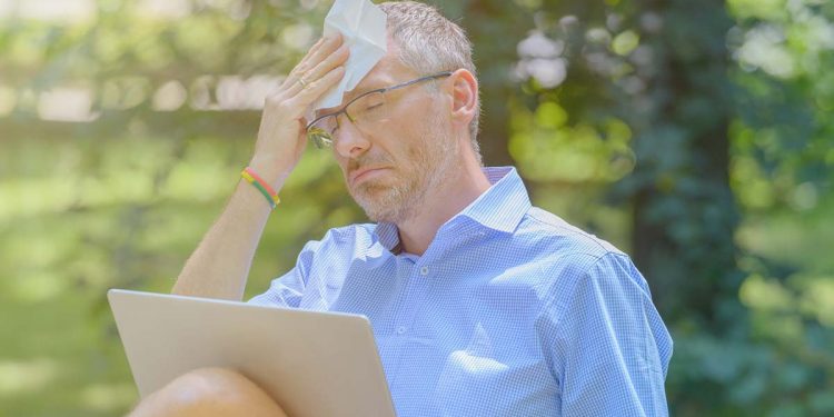 Man suffers from heat while working with laptop