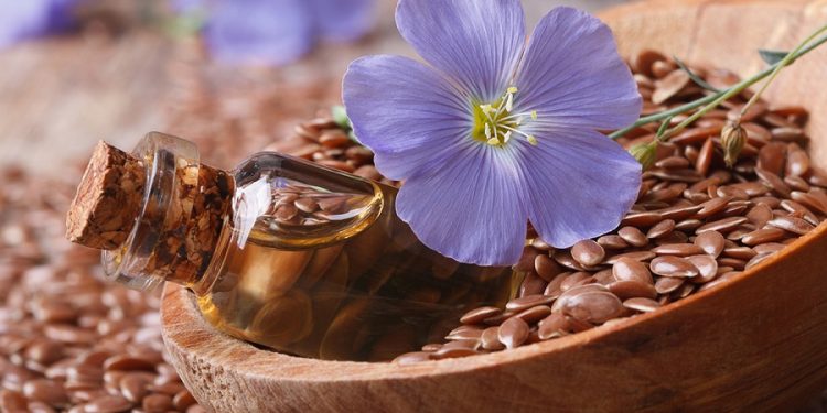 flax oil in a glass bottle, flowers and seeds in a spoon macro