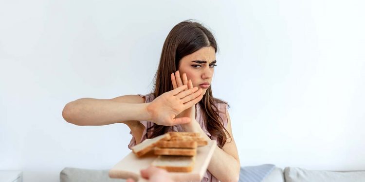 Cropped shot of a young woman on a gluten free diet is saying no thanks to white bread. Woman refusing to eat white bread. Gluten intolerance concept. Health care and medicine concept. Copy space.