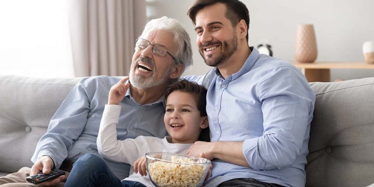 Happy three generation men family hold remote control watch tv