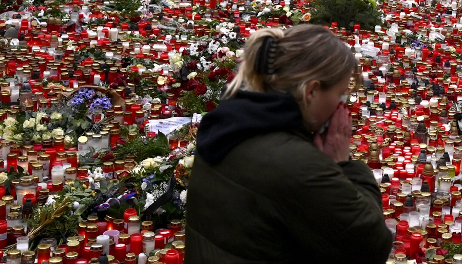 A young woman reacts by the floral tributes and candles left outside the headquarters of Charles University in downtown Prague, Czech Republic, Saturday, Dec. 23, 2023. A lone gunman opened fire at a university on Thursday, killing over 12 people and injuring dozens. (AP Photo/Denes Erdos)