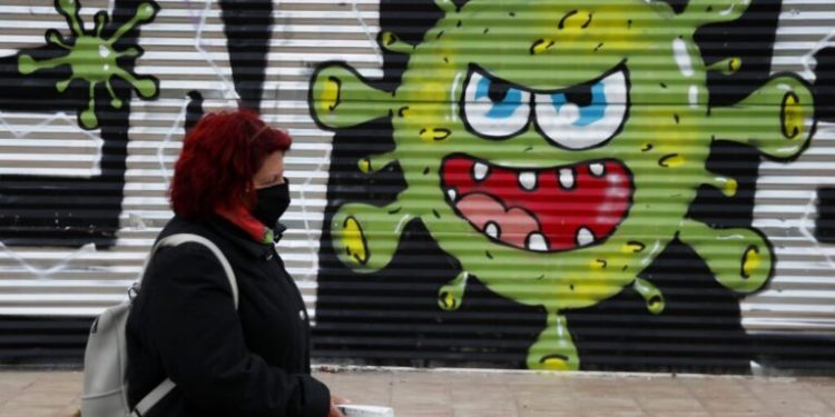 A woman wearing a face mask to prevent the spread of coronavirus, walks in front of a graffiti by artists Open/Esem in Athens, Tuesday, Jan. 12, 2021. Greece has extended a two-month lockdown till Jan. 18, and announced plans to increase the number of people getting COVID-19 vaccines. (AP Photo/Thanassis Stavrakis)
