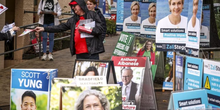 Volunteers hand out voting cards next to election candidate posters outside a pre-polling centre in Sydney on May 2, 2025, ahead of Australias federal election scheduled for May 3. (Photo by DAVID GRAY / AFP)